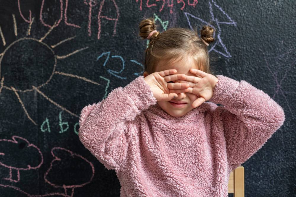 menina triste na creche a tapar o rosto