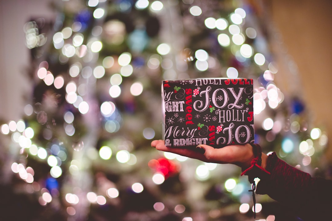 mão feminina a segurar um presente embrulhado com árvore de natal iluminada no fundo